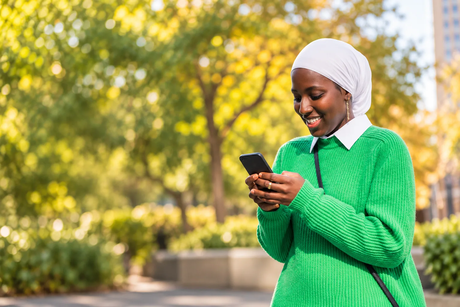 A smiling woman in a white headscarf using her phone outdoors